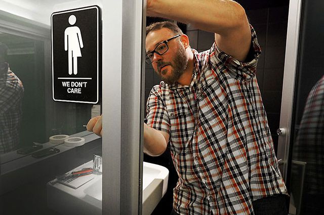 A hotel manager adheres informative backing to gender neutral signs in the 21C Museum Hotel public restrooms on May 10, 2016 in Durham, North Carolina